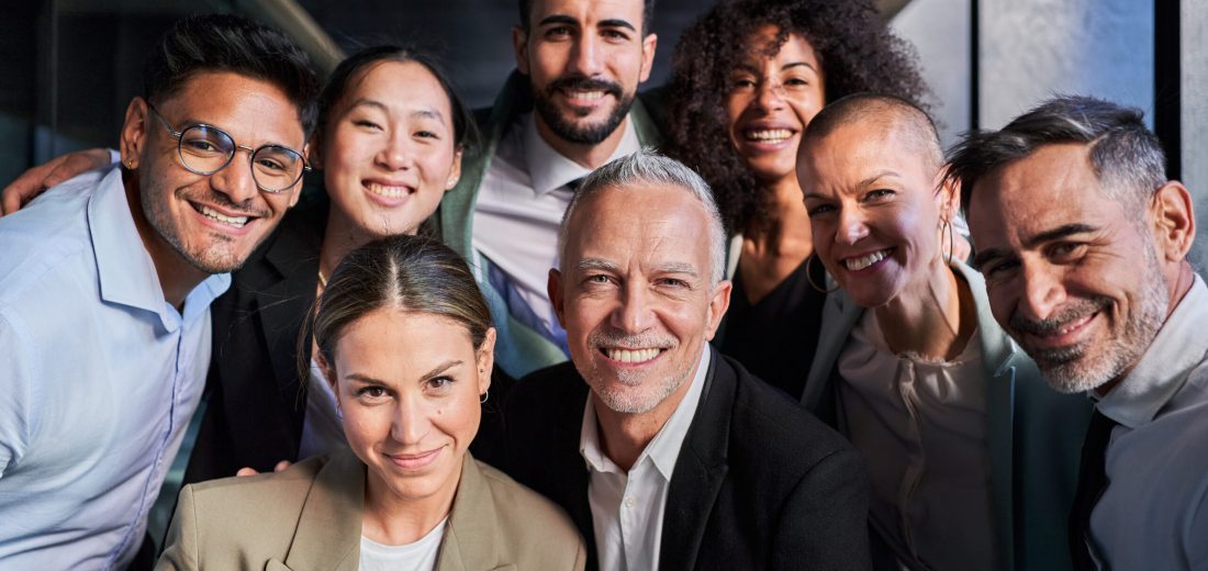 Cheerful portrait of a group of business colleagues taking a photo for the company page in the office, gathered looking at camera smiling, headed by the boss. Startup concept.